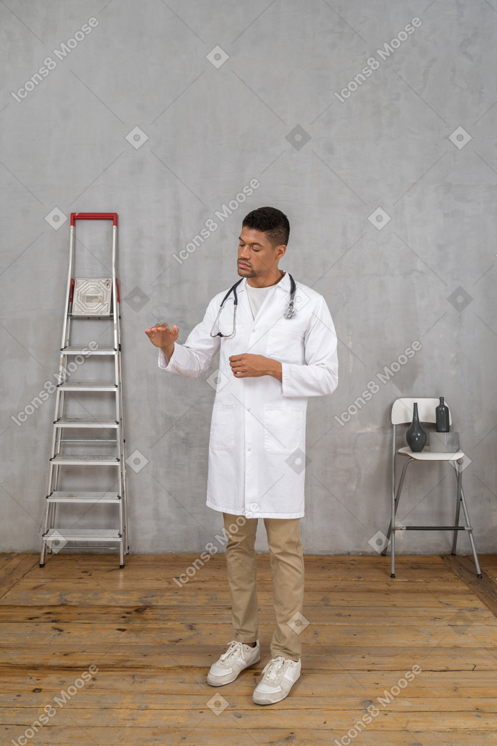 Dreiviertelansicht eines jungen arztes, der in einem raum mit leiter und stuhl steht und eine größe von etwas zeigt
