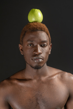Close-up unemotional young male with an apple on his head