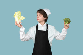 Kid boy chef holding chinese cabbage and broccoli
