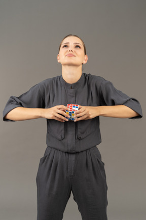 Vista frontal de una mujer joven en un mono tratando de resolver el rompecabezas del cubo de rubik