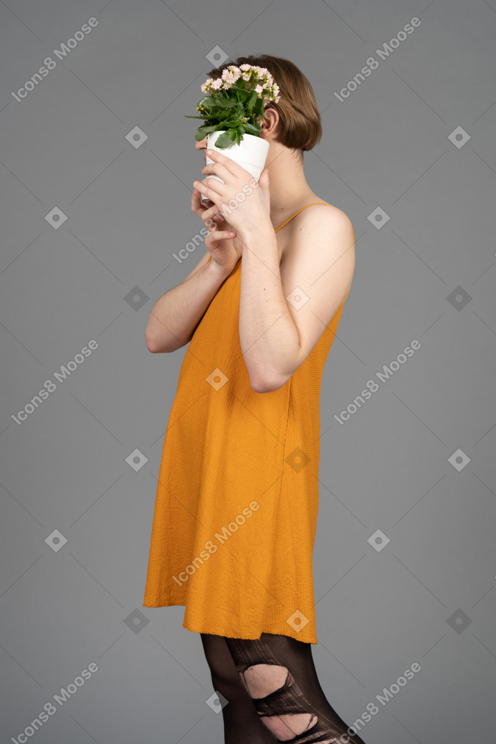 Side view of a person in orange dress covering face with flower pot