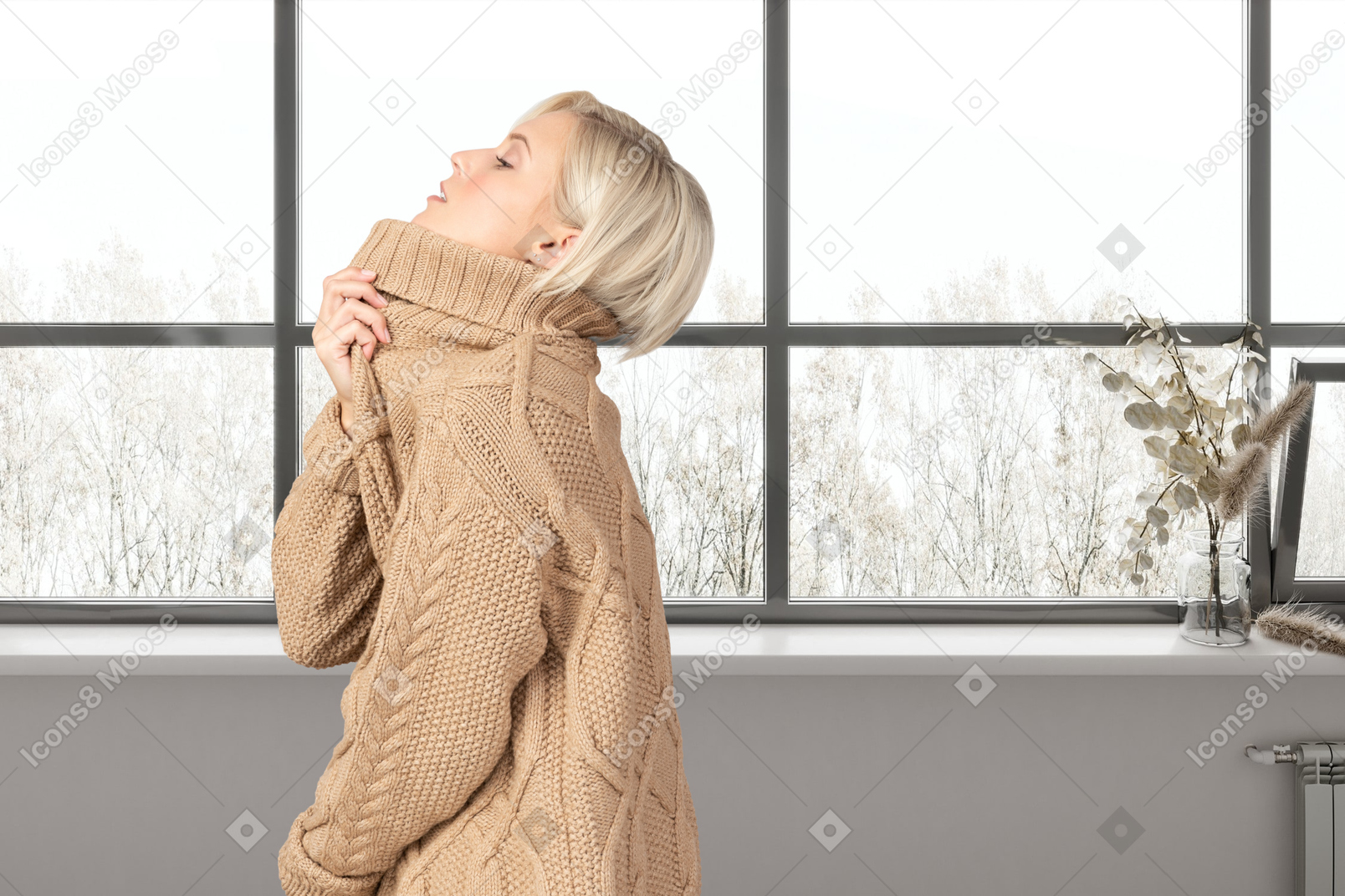 창문 근처에 서 있는 따뜻한 스웨터를 입은 여자