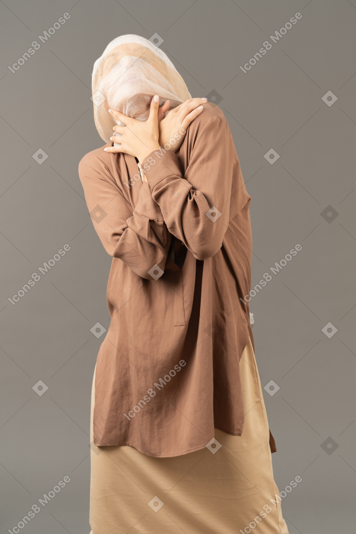 Женщина с покрытой головой держится за шею обеими руками