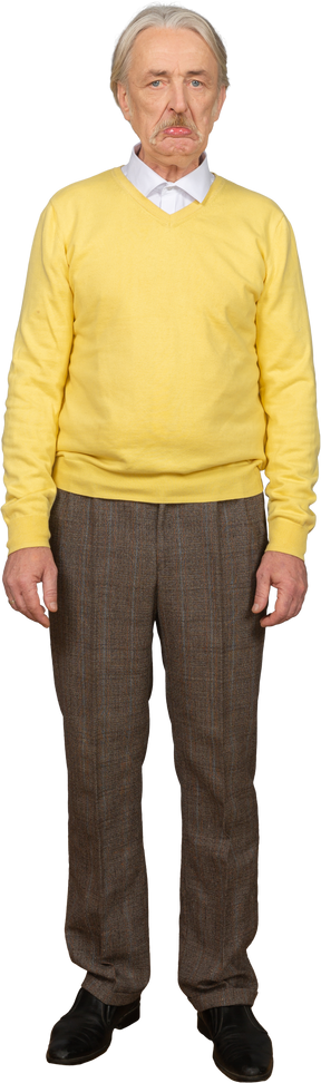 Vista frontal de um velho descontente com uma camisola amarela a olhar para a câmara