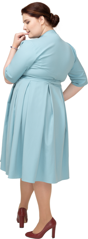 Vista posteriore di una donna in abito blu che si morde il dito