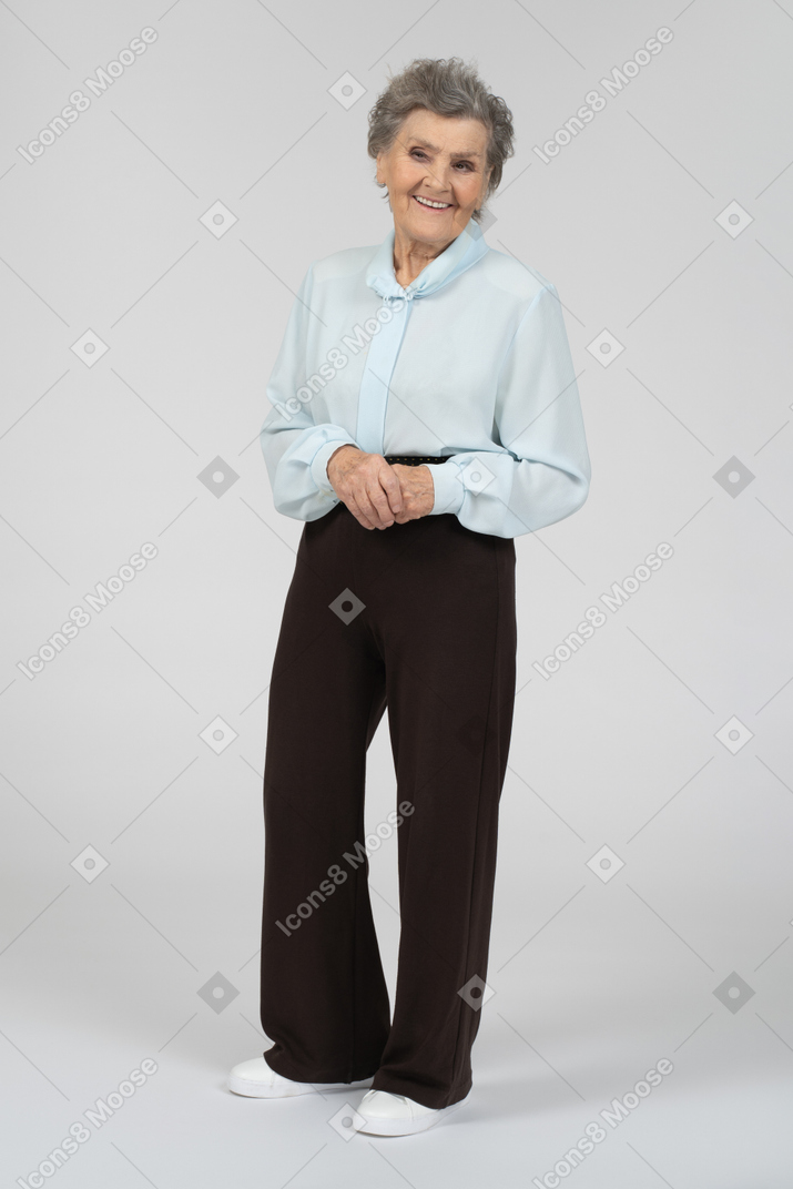 Vue de trois quarts d'une vieille femme souriant brillamment avec les mains jointes