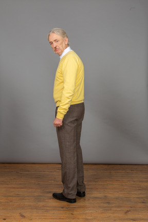 Side view of a displeased old man in a yellow pullover looking at camera