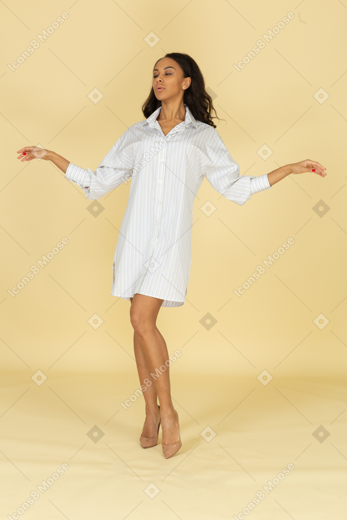 Вид спереди темнокожей молодой женщины в белом платье, протягивающей руки