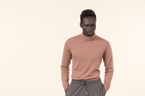 A young black man in a beige turtleneck and grey sweatpants standing casually on the white background