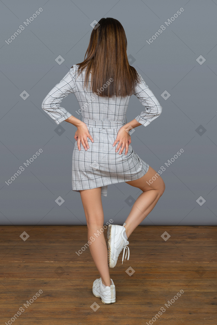 Slim brunette woman holding hands on hips back to camera