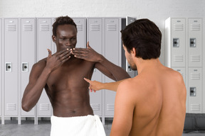 Two men in towels joking around in a locker room