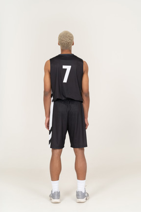 Vista traseira de um jovem jogador de basquete, parado e olhando para cima