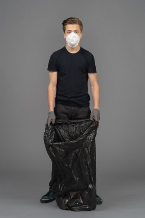 A young man wearing a mask while holding a trash bag