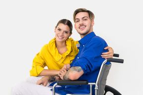 Young woman is holding her boyfriend in a wheelchair and smiling