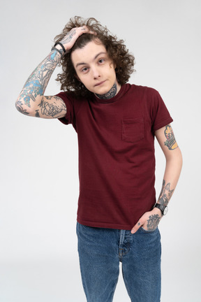 Adolescente tatuado sosteniendo su cabello castaño rizado con una mano
