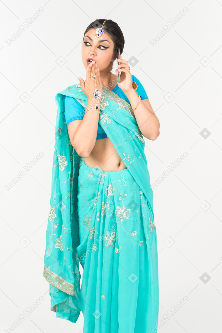 Young indian dancer in blue sari closing mouth and talking on the phone