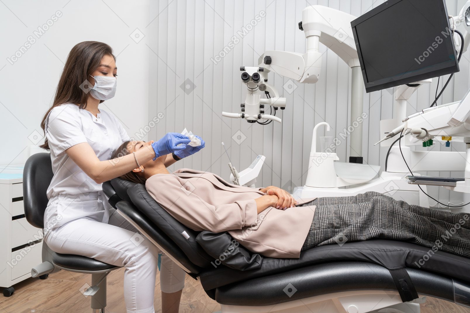Full-length of a female dentist examining her patient in a hospital cabinet and holding a napkin