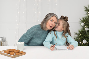 A woman and a little girl sitting at a table in front of a christmas tree