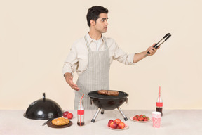 Joven hombre caucásico gritando algo mientras prepara barbacoa