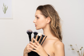 Vue de trois quarts d'une jeune femme sensuelle tenant des pinceaux de maquillage