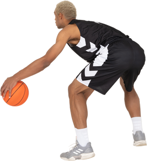 ドリブルをしている若い男性のバスケットボール選手の4分の3の背面図
