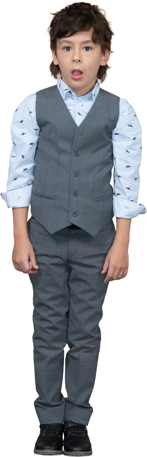 Vista frontal de un chico lindo en traje gris de pie con la boca abierta