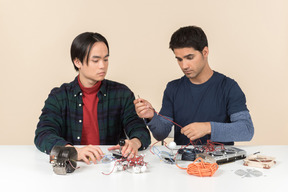 Dois jovens geeks sentado à mesa e consertando alguns detalhes