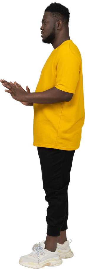 그의 팔을 뻗은 노란색 티셔츠에 젊은 검은 피부 남자의 측면보기