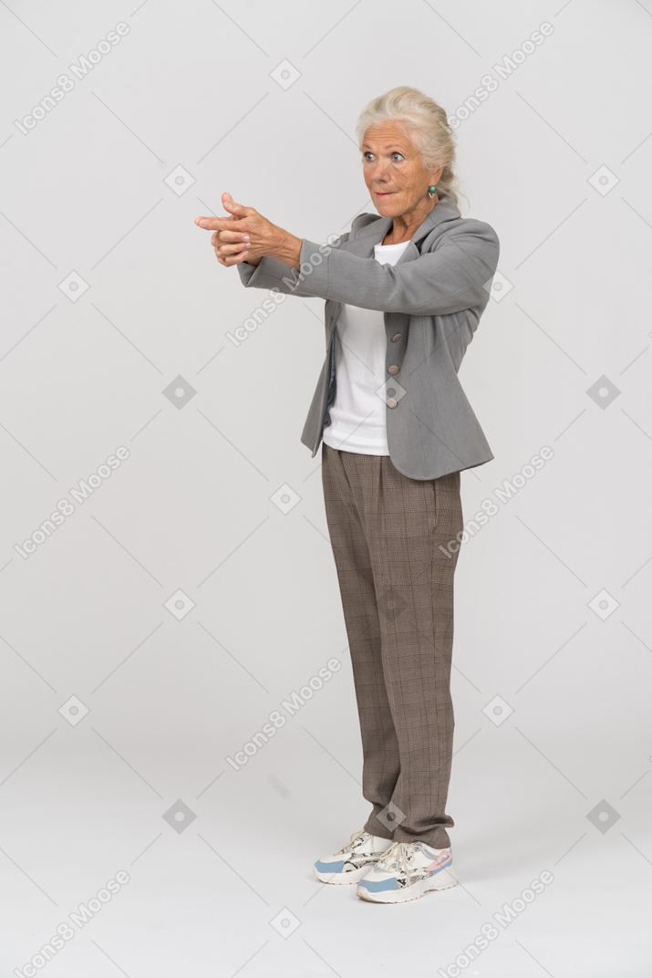 Вид сбоку пожилой дамы в костюме, показывающей пистолет с пальцами
