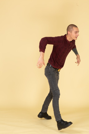 Three-quarter view of a walking young man in red pullover raising hands