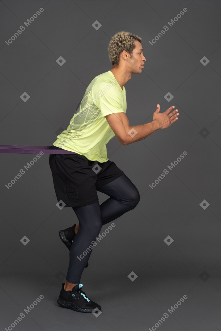 Side view of a dark-skinned young man running with an elastic rubber