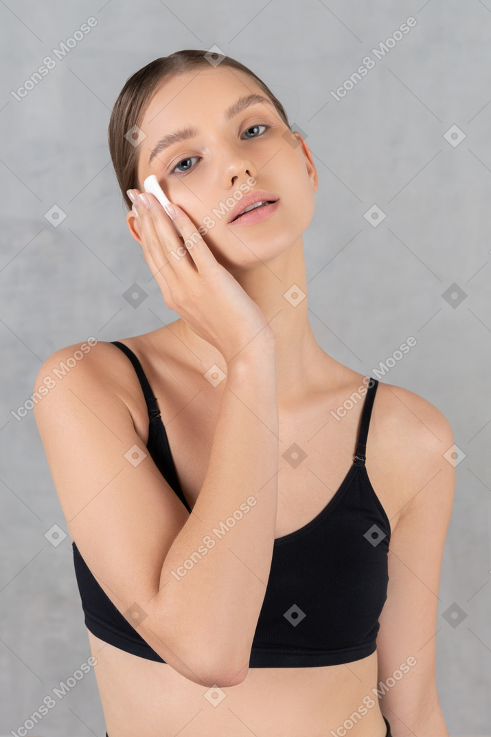 Attractive young woman removing makeup from her face with cotton pad