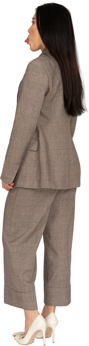 Three-quarter back view of a young lady in brown business suit showing tongue