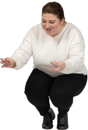 Front view of a happy plump woman in casual clothes squatting