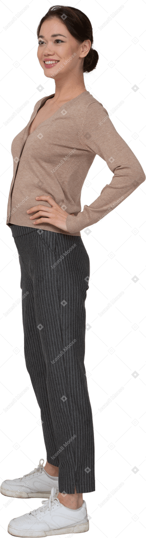 Vista di tre quarti di una giovane donna sorridente in pullover e pantaloni mettendo le mani sui fianchi
