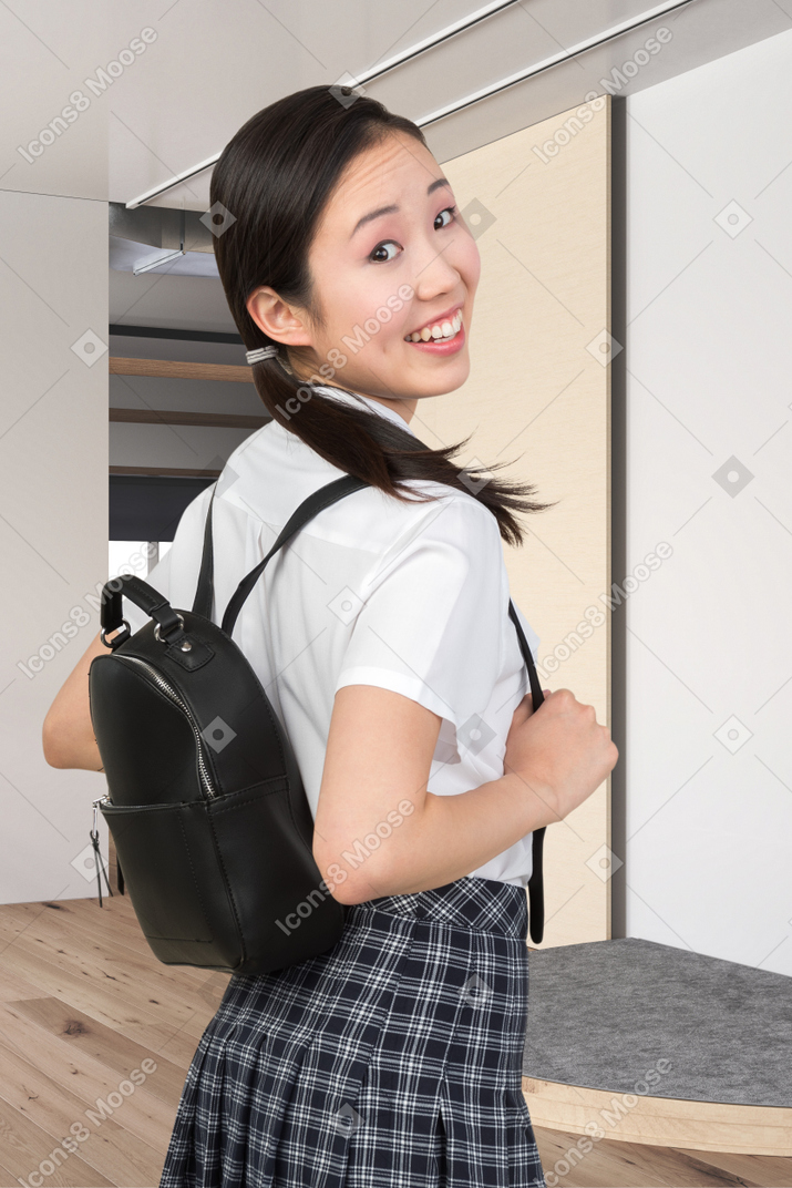 A young girl in a school uniform holding a backpack