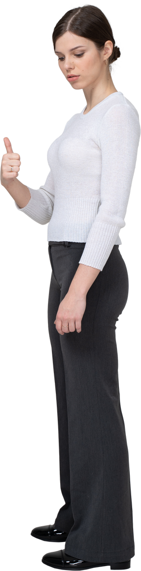 Side view of a cheerful young woman in office clothing showing thumb up