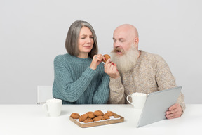 Aged couple having cookies and looking at tablet