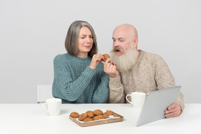 Couple âgé ayant des cookies et regardant tablette