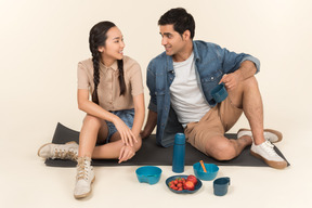 Interracial couple sitting on karimat near dishes