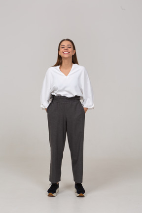 Vista frontal de una joven sonriente en ropa de oficina poniendo las manos en los bolsillos