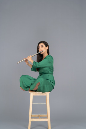 Full-length of a young lady playing the clarinet sitting with her legs crossed on a wooden chair