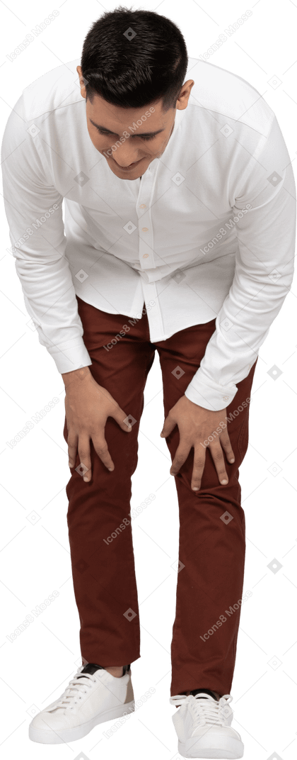 Vista frontal de un joven latino inclinado hacia adelante y apoyando las manos sobre las rodillas con una sonrisa