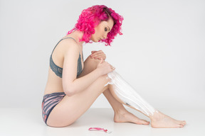 Young woman sitting on the floor and applying shaving cream