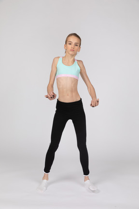 Вид спереди девушки-подростка в спортивной одежде, поднимающей руки и ногу во время танца