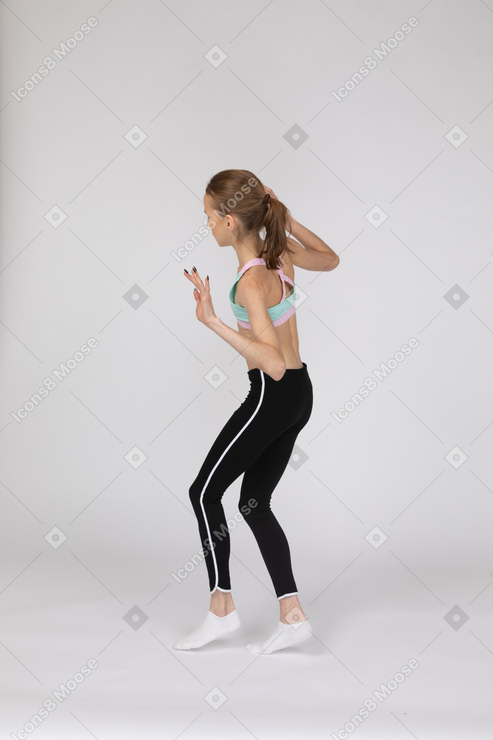 Vista posterior de tres cuartos de una jovencita en ropa deportiva caminando cautelosamente de puntillas