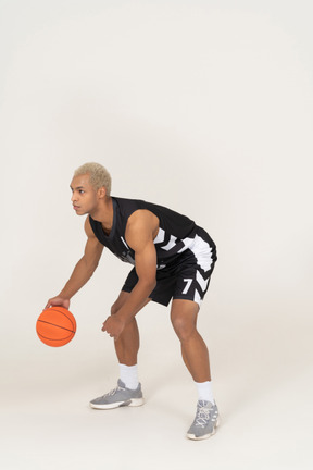 Вид в три четверти молодого баскетболиста мужского пола, ведущего дриблинг