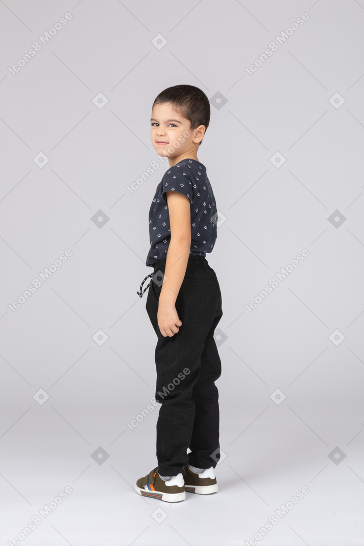 Vista lateral de um menino com roupas casuais olhando para a câmera e fazendo caretas