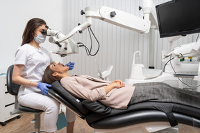 Comprimento total de uma dentista curando sua paciente e olhando através do microscópio