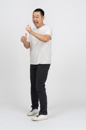 Vista frontal de um homem alegre em roupas casuais, mostrando os polegares